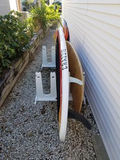 two surfboards leaning against the side of a house next to some plants and gravel