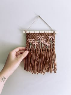 a hand holding a piece of woven material with flowers and leaves on it, in front of a white wall