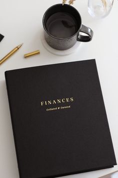 a black book sitting on top of a white table next to a cup of coffee