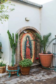 an outdoor courtyard with potted plants and a virgin mary painting on the wall behind it