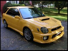 the yellow car is parked on the side of the road in front of some trees