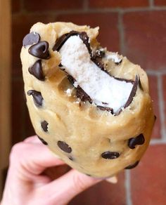 a person holding up a cookie doughnut with chocolate chips and marshmallows