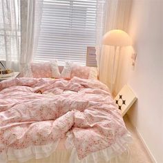 a bed with pink and white comforter next to a window