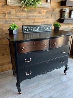 a black dresser with a sign that says everyday counts on it and some potted plants