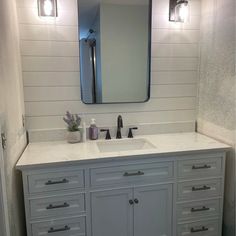 a white bathroom vanity with two sinks and a large mirror above it, along with three lights on either side of the sink