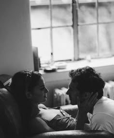 a man and woman sitting next to each other on a couch in front of a window