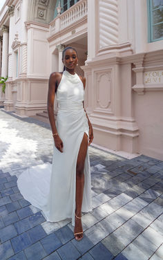 a woman standing in front of a pink building wearing a white dress and high heels