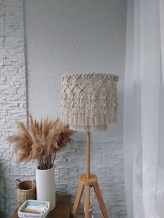 a wooden table topped with a lamp next to a vase filled with dried flowers and plants