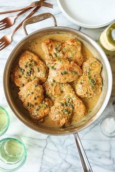 a pan filled with meat covered in sauce and garnished with herbs next to silverware