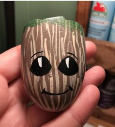 a hand holding a painted rock with a smiling face on it in front of a shelf