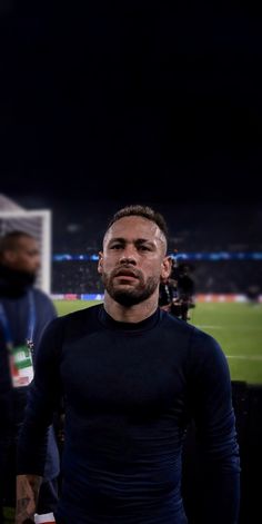 a man standing in front of a soccer field at night with other players behind him