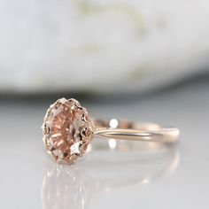 an engagement ring with a pink diamond in the center on a white surface, next to a rock