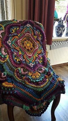 a colorful crocheted blanket sitting on top of a wooden chair next to a window