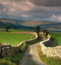 a dirt road going through a lush green field next to a stone wall and gate