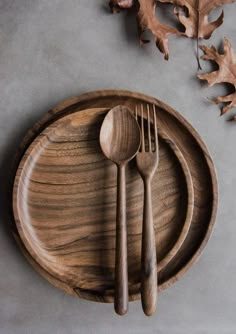 a wooden plate with two forks and spoons on it next to an oak leaf