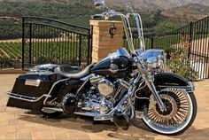 a black and chrome motorcycle parked in front of a fenced area with mountains behind it