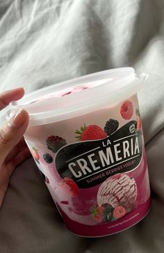 a hand holding a cup of ice cream with strawberries and raspberries on it