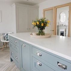 a kitchen with blue cabinets and yellow flowers in a basket on the counter top,