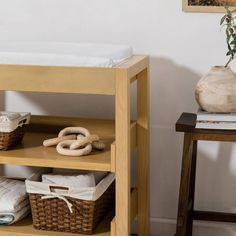 a baby changing table with baskets and blankets on the top shelf, next to a potted plant