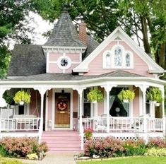 a pink and white house with flowers on the front porch is surrounded by greenery