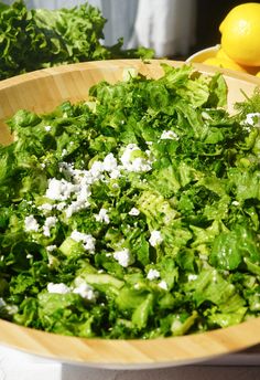 a wooden bowl filled with lettuce next to lemons