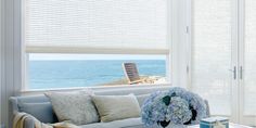 a living room filled with furniture and windows covered in white blinds next to the ocean