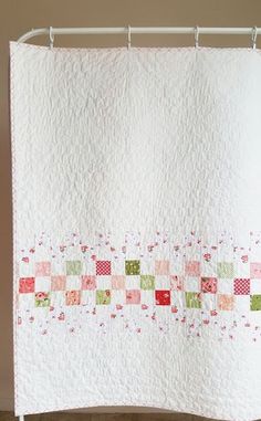 a white quilt hanging on a shower curtain with pink and green squares in the center