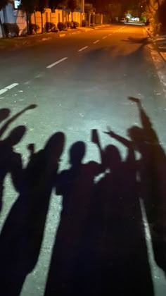 the shadow of several people holding their hands up in the air on a street at night