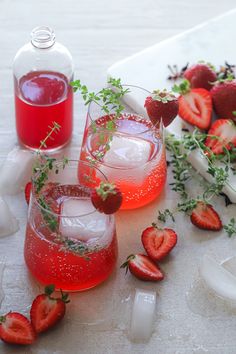 two glasses filled with liquid and strawberries next to ice cubes on a table