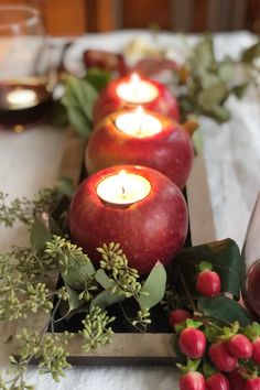 some apples are sitting on a table with candles and greenery in front of them