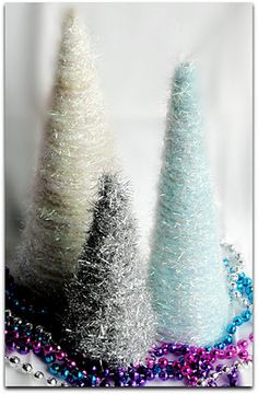 three silver and white christmas trees are on a table with beaded necklaces around them