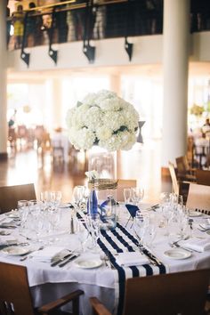 a dining room table is set with white flowers and wine glasses for an elegant centerpiece