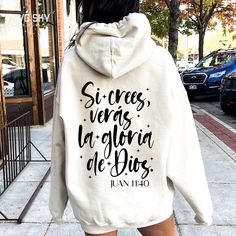 a woman walking down the street wearing a white hoodie with writing written on it