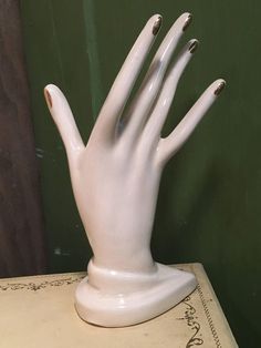 a white ceramic hand sculpture sitting on top of a table next to a green wall