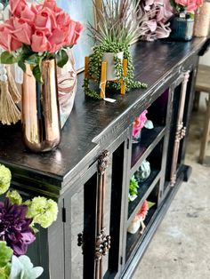 several vases with flowers are on top of a black shelf in front of a wall