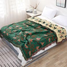 a bed with a green blanket on top of it next to a white nightstand and window