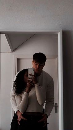 a man and woman standing in front of a mirror taking a selfie with their cell phone