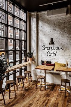 an empty restaurant with wooden tables and stools in front of large windows that look out onto the street