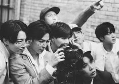 black and white photograph of young men taking pictures with cameraman in front of brick wall