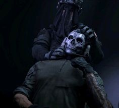 a man with a skeleton face and helmet on holding another person's head in the dark