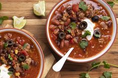 two bowls of chili with sour cream and black olives on a wooden cutting board