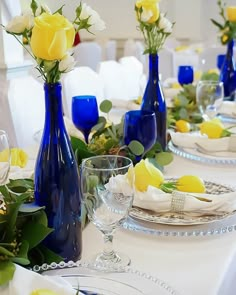 the table is set with blue vases and yellow roses in them, along with other place settings