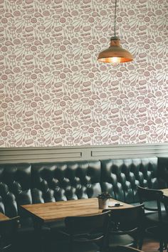 an empty booth with black leather seats and wooden tables in front of a wallpapered wall