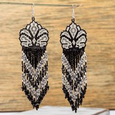 the black and white beaded earrings are hanging from a metal hook on a wooden surface