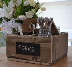 a wooden box with forks and spoons in it on a table next to flowers