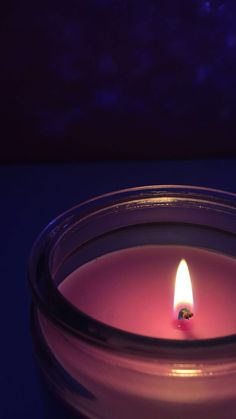 a lit candle sitting on top of a table next to a purple wall and floor