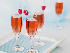 three glasses of wine with raspberries in them on a white tray and blue background