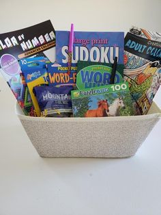 a white basket filled with books on top of a table next to a cup full of pens