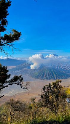 a view of a mountain with some clouds in the sky and trees on the ground