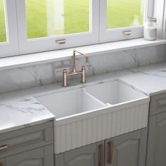 a kitchen with marble counter tops and double sinks in front of two windows that look out onto a grassy field